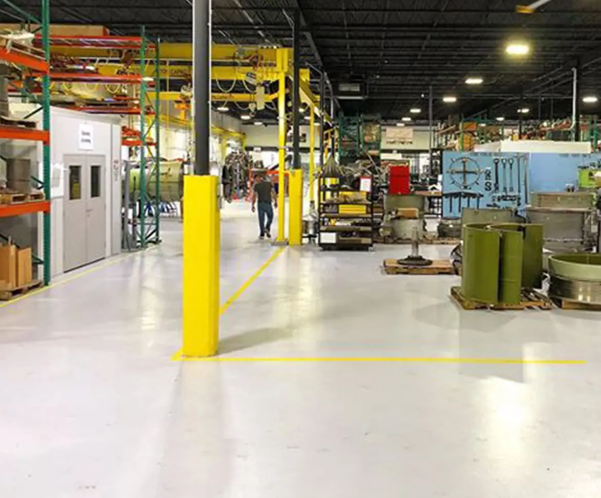 SPF Industrial crew applying epoxy flooring under heavy machinery in a manufacturing facility