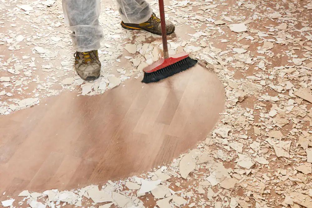 Worker sweeping up VCT tile debris after professional removal